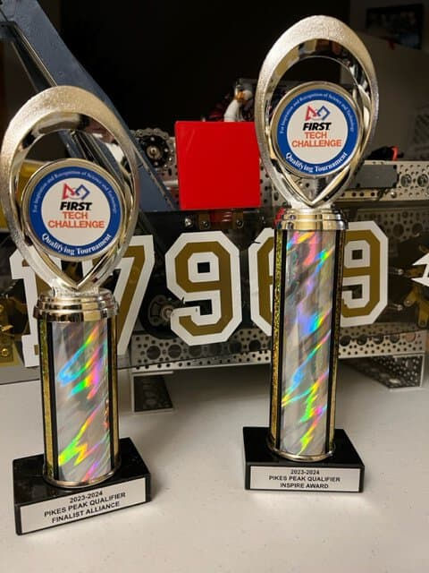 Two 2023-2024 Pikes Peak Qualifier robotics awards (finalist alliance and inspire award) side by side in front of a robot made by students.