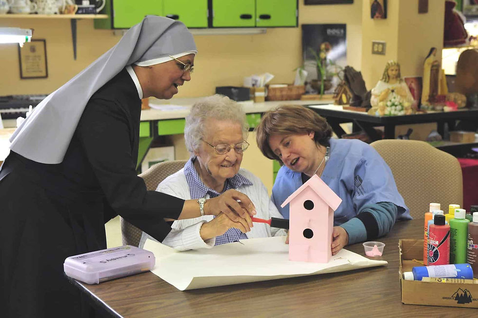 A nun from the Little Sisters of the Poor helps older woman paint a pink birdhouse