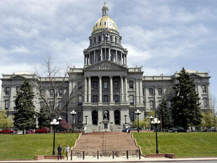 Historic building with a gold dome, set against a cloudy sky. Two people walk on steps, flanked by trees and classic lamps. Peaceful mood.