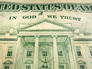 Close-up of a U.S. dollar bill showing the White House, with IN GOD WE TRUST and green engraved details.