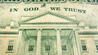 Close-up of a U.S. dollar bill showing the White House, with IN GOD WE TRUST and green engraved details.
