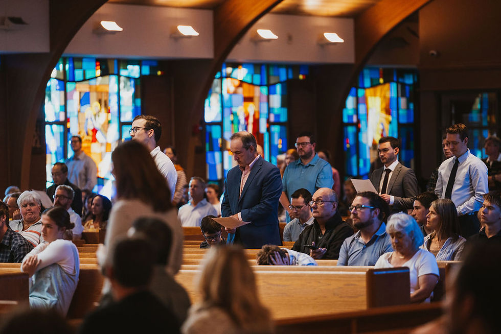 Church congregation stands in wooden pews, reading papers before stained-glass windows in a quiet, solemn service.