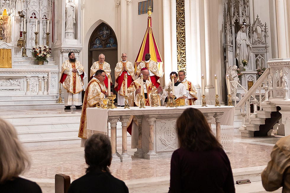 Priests in gold vestments celebrate Mass at an ornate white church altar, with congregants seated in the foreground.