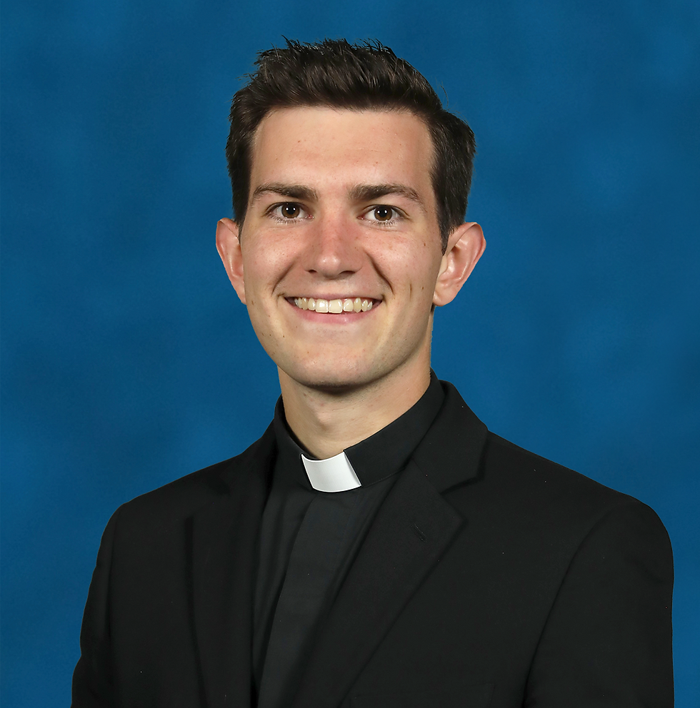 Smiling young priest in a black suit and clerical collar against a blue studio background.