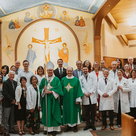 Large group of clergy, doctors, and parishioners posing in a church under a crucifix mural.