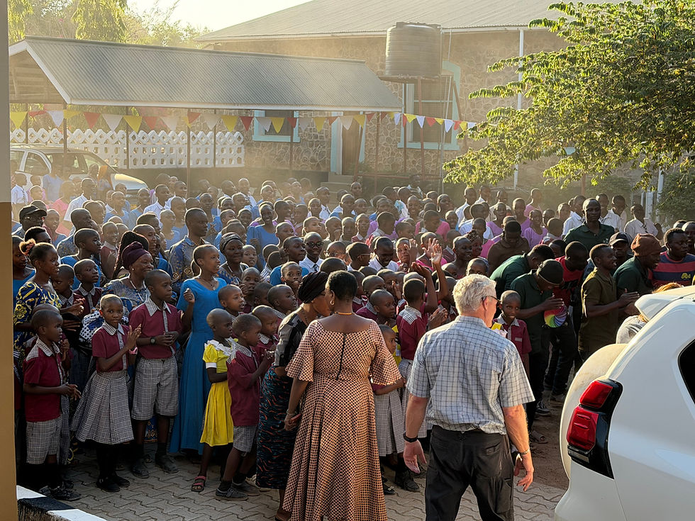 Crowded outdoor school gathering of children and adults in uniforms applauding near a stone building with bunting in warm sunlight.