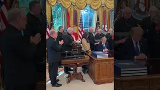 Donald Trump bows his head at the Resolute Desk in the Oval Office while bishops pray over him among U.S. flags and gold drapes.