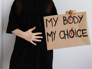 Person in black holds a cardboard sign reading MY BODY MY CHOICE with red lightning marks, against a white wall.