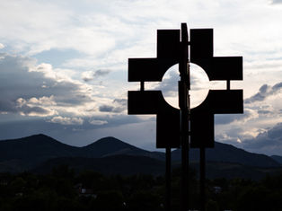 Silhouetted geometric sign against cloudy dusk sky, with mountains and trees in the background.