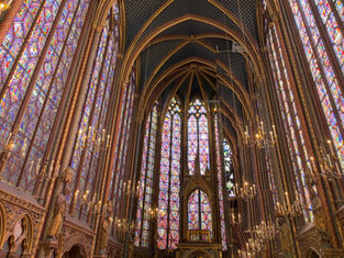 Ornate Gothic chapel interior with tall stained-glass windows, arched ceilings, and glowing chandeliers, bathed in colorful light.
