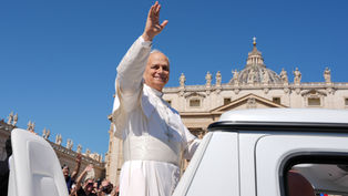Pope in white waves from an open vehicle outside St. Peter’s Basilica as crowds cheer under a clear blue sky.