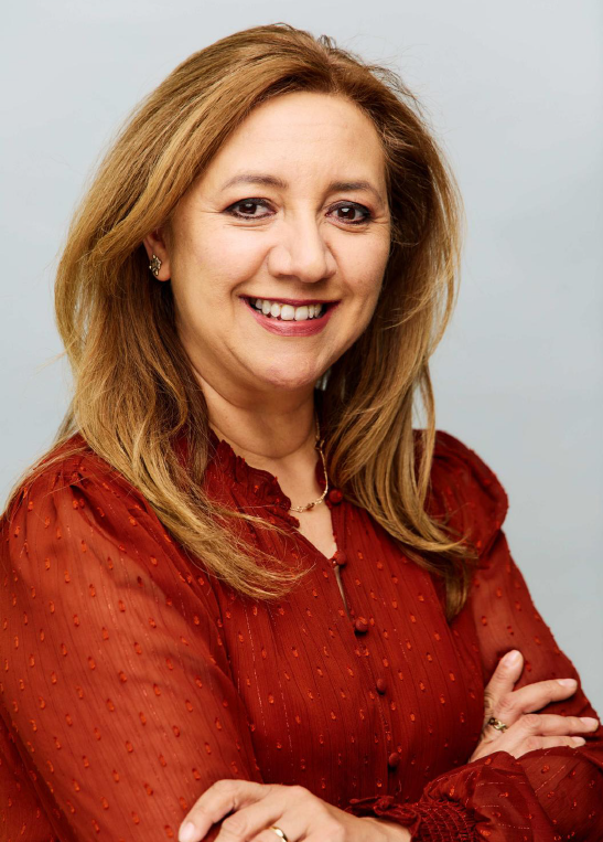 Smiling woman in a red blouse with crossed arms, posed against a light gray background.