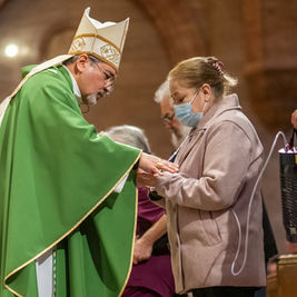 Bishop in green vestments blesses a masked woman during a church service.