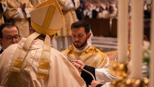 Catholic ordination ceremony with bishop in gold vestments and a kneeling man receiving a paten in a church