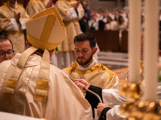 Catholic ordination ceremony with bishop in gold vestments and a kneeling man receiving a paten in a church