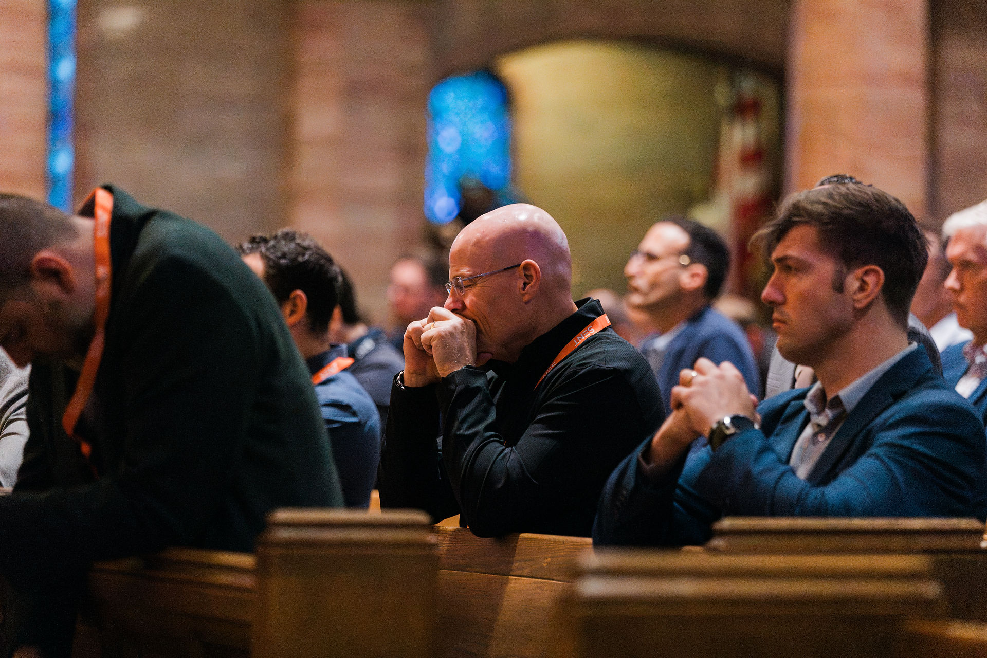 Men in professional attire kneel during a church service. The mood is reflective and peaceful.