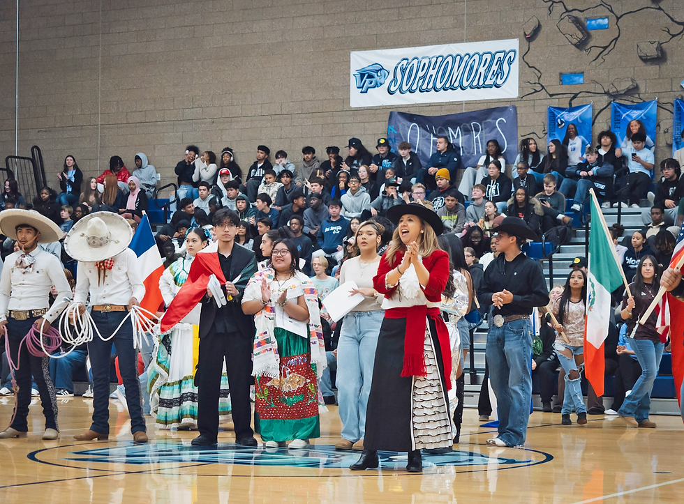 Students in cultural dress and sombreros clap in a gym, holding flags under a Sophomores banner.