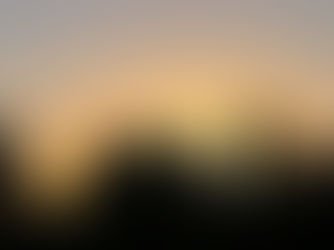 Silhouetted church bell tower with cross above trees at sunset, glowing orange sky and calm evening mood.