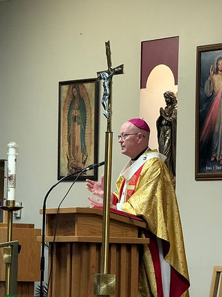 Bishop in gold vestments speaks at a church lectern, with a crucifix and Marian artwork behind him.
