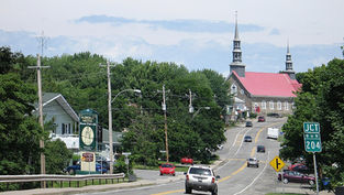 Small town street with cars driving toward a red-roofed church, trees and motel signs along a winding road, route 204.
