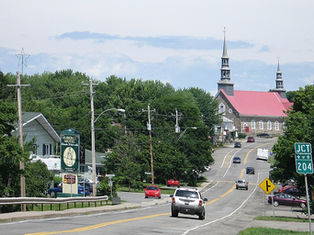 Small town street with cars driving toward a red-roofed church, trees and motel signs along a winding road, route 204.