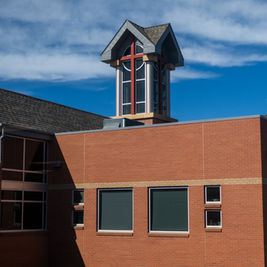 Red brick church building with a tall cross-topped tower under a blue, cloud-streaked sky