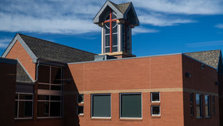 Red brick church building with a tall cross-topped tower under a blue, cloud-streaked sky