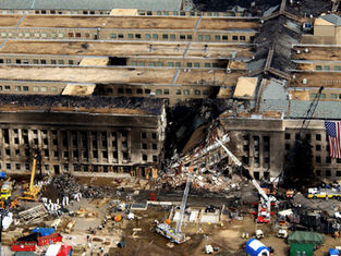 Burned Pentagon section with collapsed center, rescue crews and cranes below, American flag hanging on right, aftermath scene