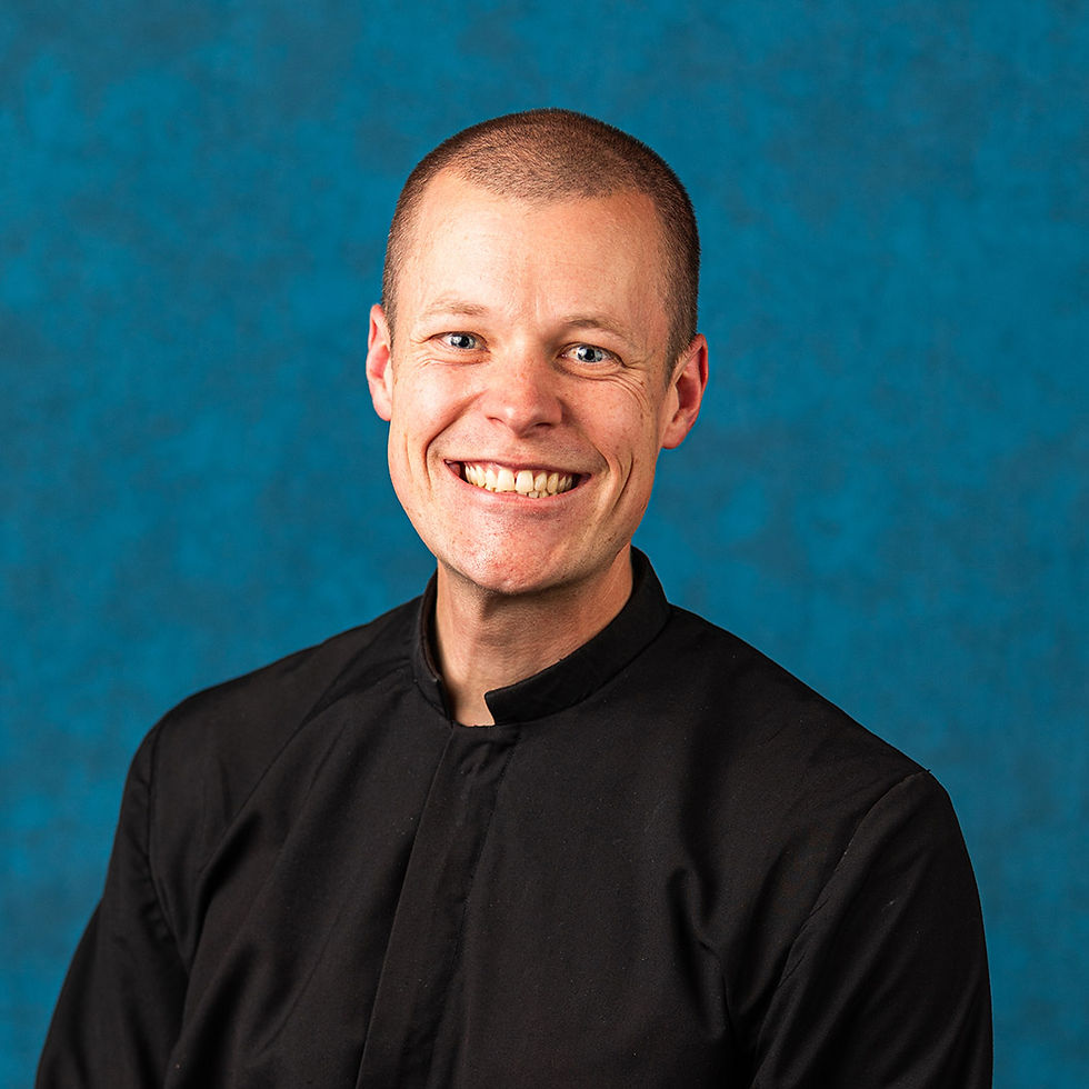 Smiling man in a black shirt poses against a blue studio backdrop.