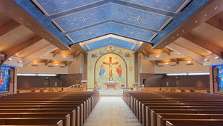 Empty church sanctuary with wooden pews, blue painted ceiling, stained glass, and a crucifix mosaic over the altar