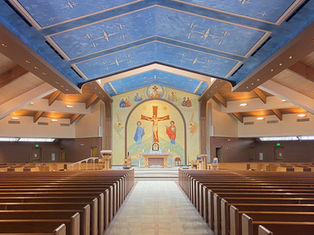 Empty church sanctuary with wooden pews, blue painted ceiling, stained glass, and a crucifix mosaic over the altar