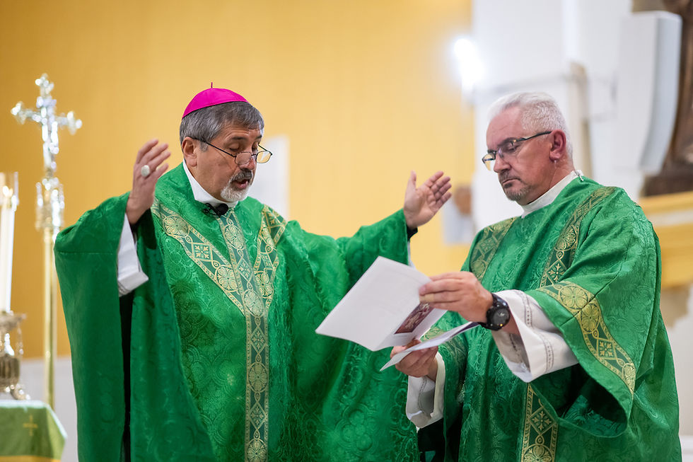 Two priests in green vestments confer at the altar, one gesturing while the other reads from papers in a church.