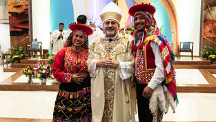 Smiling trio in colorful traditional dress pose inside a church altar; banners read Thanks to the LORD.