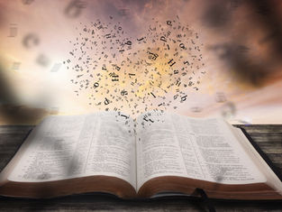 Open Bible on a wooden table with black letters rising into a cloudy sunset sky, suggesting inspiration and reverence