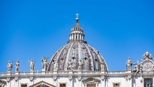 St. Peter’s Basilica dome and statues against a clear blue sky, with a clock on the right and no people visible.