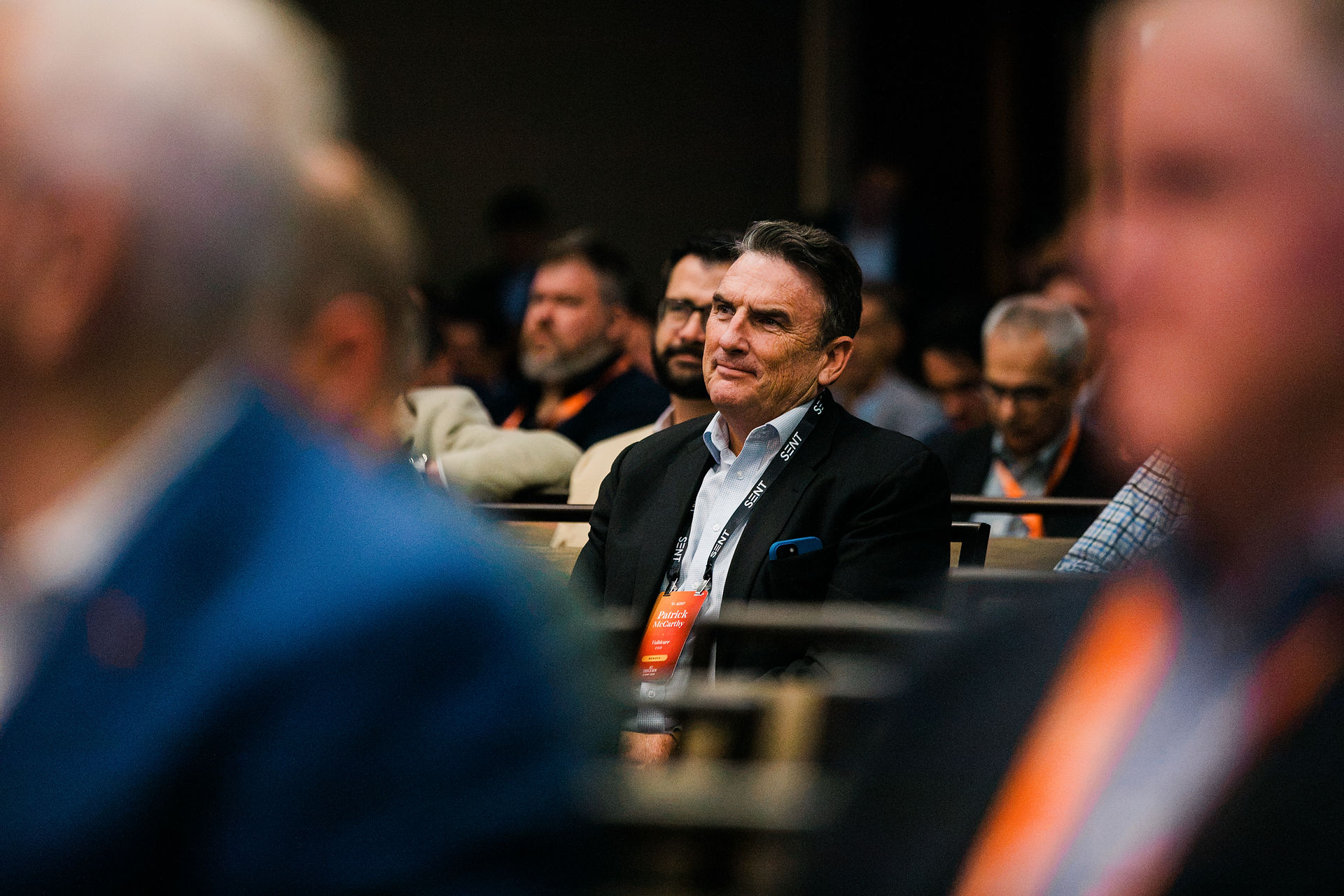 Men in suits sit in a conference hall listening attentively.