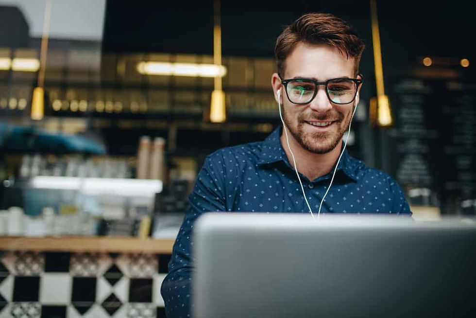 A man with glasses and earbuds is focused on writing a Denver Catholic article on his laptop.
