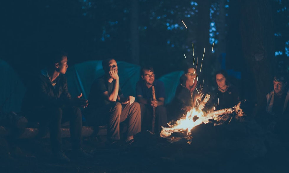 A circle of friends gathers around a campfire at night, illuminated by firelight, sharing faith and fellowship.