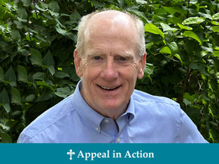 Smiling man in a blue shirt stands in front of lush green foliage. Text below reads "Appeal in Action" with a cross symbol.
