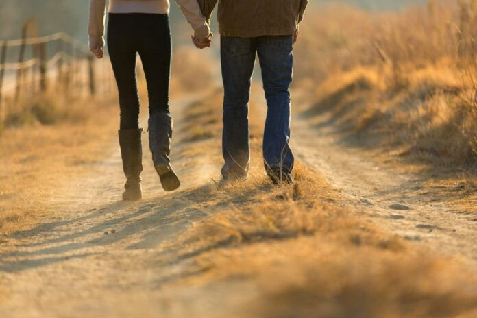 young couple holding hands walking on autumn rural path in the morning (Photo: Adobe Stock)