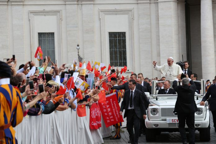Pope Francis rides by a crowd holding many flags