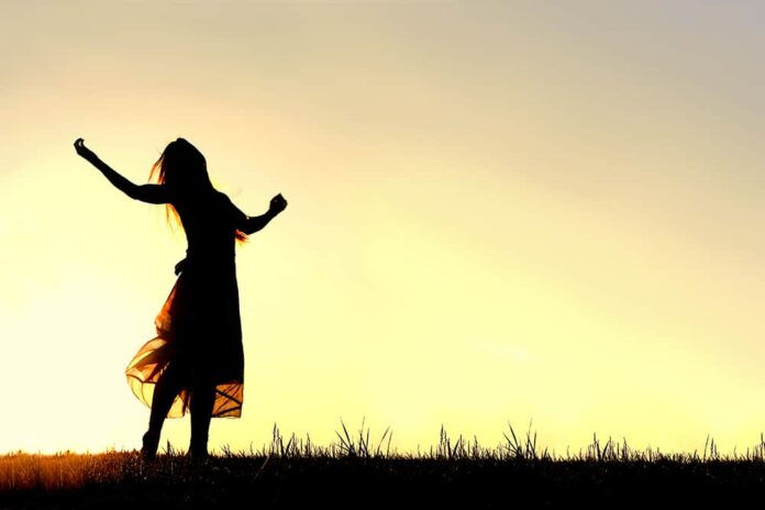 A woman wearing a long skirt, with long blonde hair, is dancing and praising God, while silhouetted against the evening sky (Photo: Adobe Stock)