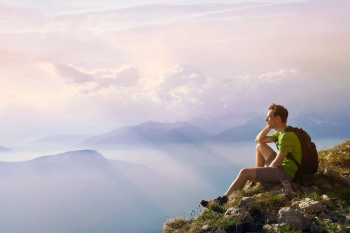 man sitting on top of mountain, achievement or opportunity concept, hiker looking forward on beautiful panoramic landscape (Photo: Adobe Stock)