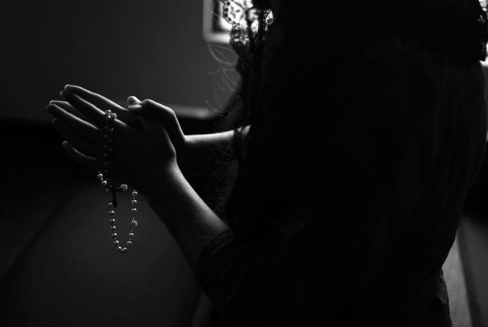 Woman with prayer hands holding a rosary