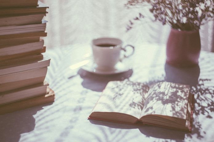 Open book on table with coffee mug and vase