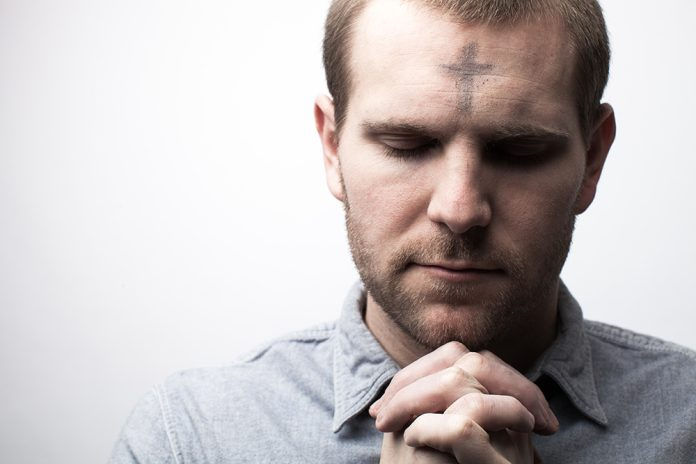 Man praying with a cross made of ashes on his forehead