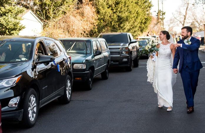 DENVER, CO - APRIL 17: Ashley Stratman and Ryan Bradshaw walk by a line of their friends, safely remaining in their individual cars, who drove to Our Lady of Lourdes Catholic Church to congratulate the couple following their pared down wedding ceremony on April 17, 2020, in Denver, Colorado. (Photo by Anya Semenoff/Denver Catholic)